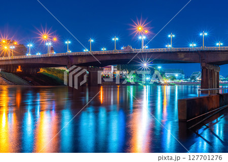 Beautiful lights water reflection full of banks of the Nan River at night on the bridge (Naresuan Bridge)at night in the park in Phitsanulok City,Thailand. Beautiful lights water reflection full of banks of the Nan River at night on the bridge (Naresuan Bridge)at night in the park in Phitsanulok City,Thailand. 127701276