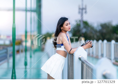 Portrait of beautiful athletic young asian woman in fashionable sportswear standing and with a holding the camera on Route walking jogging or ride bicycle and exercise on the bridge. 127701329