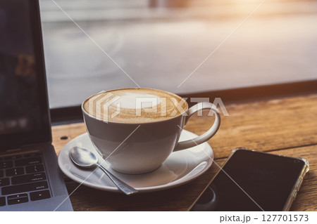 Close-up of Hot coffee latte with latte art milk foam in cup mug and laptop computer and smartphone on wood desk office desk in coffee shop at the cafe,during business work concept Close-up of Hot coffee latte with latte art milk foam in cup mug and laptop computer and smartphone on wood desk office desk in coffee shop at the cafe,during business work concept 127701573