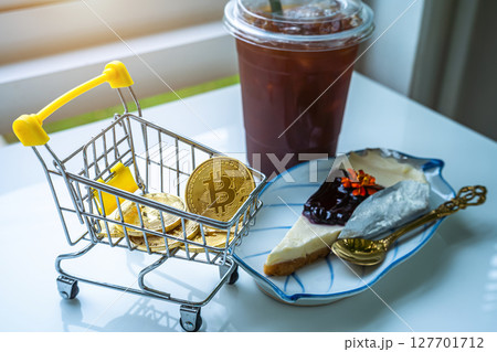 Close-up of Golden bitcoins or cryptocurrency coin or symbols in shopping cart and Americano iced coffee or black and Blueberry Cake in white table. Future currency concept. Close-up of Golden bitcoins or cryptocurrency coin or symbols in shopping cart and Americano iced coffee or black and Blueberry Cake in white table. Future currency concept. 127701712