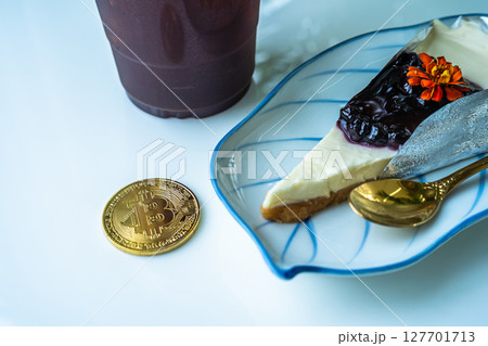 Close-up of Golden bitcoins or cryptocurrency coin or symbols and Americano iced coffee or black and Blueberry Cake in white table. Future currency concept. 127701713