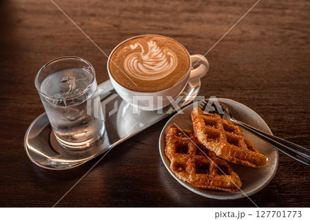 Homemade Belgian Waffles with honey and Hot coffee latte with latte art milk foam in a swan shape in cup mug on wood desk on top view. As breakfast In a coffee shop at the cafe,during business work. Homemade Belgian Waffles with honey and Hot coffee latte with latte art milk foam in a swan shape in cup mug on wood desk on top view. As breakfast In a coffee shop at the cafe,during business work. 127701773