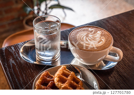 Hot coffee latte with latte art milk foam in a swan shape in cup mug and Homemade Belgian Waffles with honey on wood desk on top view. As breakfast In a coffee shop at the cafe,during business work. 127701780