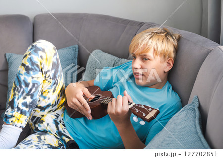 Teenager Lying on Sofa Playing the Ukulele. Relaxing at Home by Making Music. Teenager Lying on Sofa Playing the Ukulele. Relaxing at Home by Making Music. 127702851
