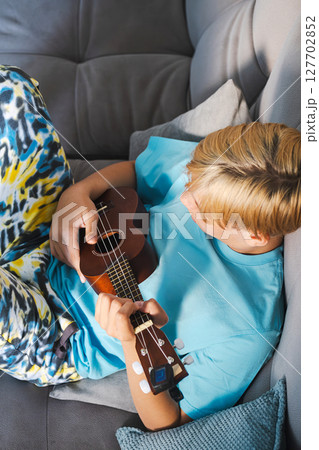 Teenager Relaxing on a Sofa, Playing a Ukulele. Learning to Play Musical Instrument Concept. 127702852