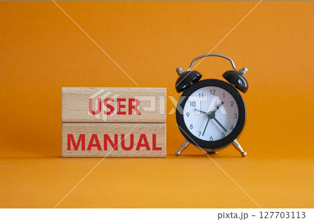 User Manual symbol. Concept words User Manual on wooden blocks. Beautiful orange background with alarm clock. Business and User Manual concept. Copy space. 127703113