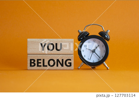 You belong symbol. Concept words You belong on wooden blocks. Beautiful orange background with alarm clock. Business and You belong concept. Copy space. 127703114