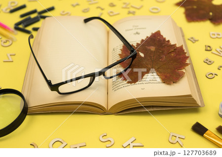 Open book with glasses on a yellow background. Autumn background associated with education.  127703689