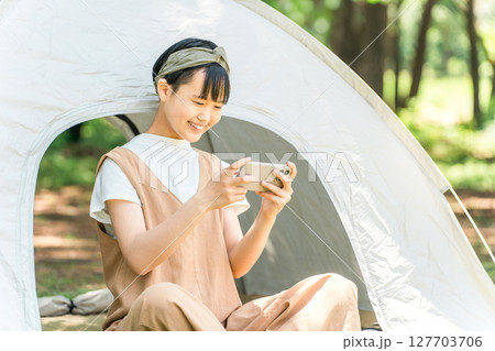 キャンプ場でテントの前でスマホを見ている女の子 キャンプ場でテントの前でスマホを見ている女の子 127703706