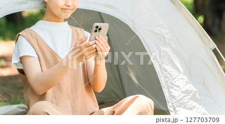 キャンプ場でテントの前でスマホを見ている女の子 キャンプ場でテントの前でスマホを見ている女の子 127703709