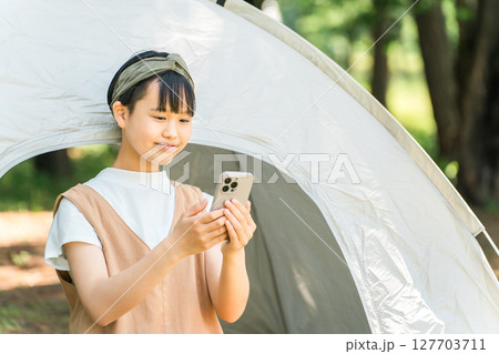 キャンプ場でテントの前でスマホを見ている女の子 127703711