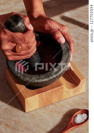 Grinding spices in stone mortar with wooden base 127703934