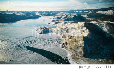 Lake Baikal in winter from the air. A freezing lake, the first ice with cracks, snow in the mountains. Lake Baikal in winter from the air. A freezing lake, the first ice with cracks, snow in the mountains. 127704114