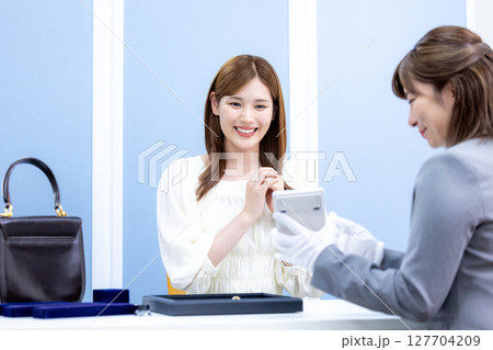 買取業者 バックと貴金属の査定をしてもらっている女性 買取業者 バックと貴金属の査定をしてもらっている女性 127704209