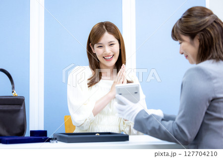 買取業者　バックと貴金属の査定をしてもらっている女性 127704210