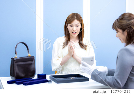 買取業者 バックと貴金属の査定をしてもらっている女性 買取業者 バックと貴金属の査定をしてもらっている女性 127704213