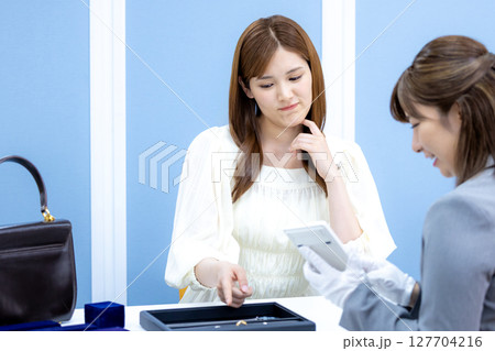 買取業者　バックと貴金属の査定をしてもらっている女性 127704216