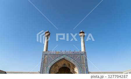 Architectural details of Minarets of Jameh Mosque of Isfahan, featuring intricate blue tilework and a pair of towering minarets against a clear sky 127704287