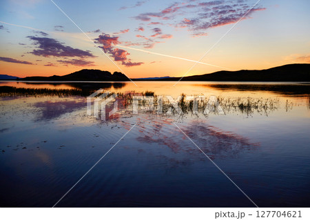 Colorful sunrise on Lake Baikal. Clouds are reflected on the surface of the water. Colorful sunrise on Lake Baikal. Clouds are reflected on the surface of the water. 127704621