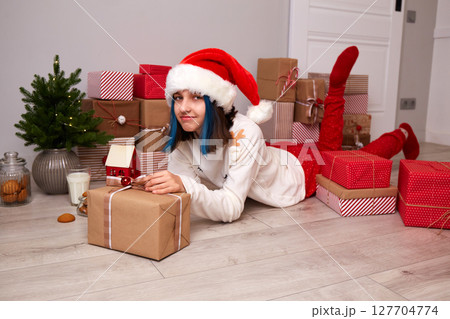A happy girl in pajamas and a Santa hat is happy with gifts for Christmas. 127704774