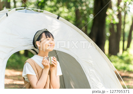 キャンプ場・レジャー施設でテントの前でドリンクを飲む女の子 127705371