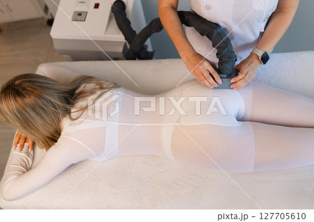Woman in special white suit getting anti cellulite massage in a spa salon. LPG, and body contouring treatment in clinic.Reset body weight with LPG massage.  127705610