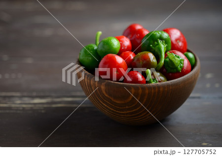 Freshly harvested red and green chili peppers arranged in a rustic wooden bowl on a dark wooden surface, showcasing vibrant colors and textures 127705752