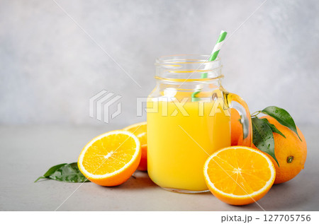 Freshly squeezed orange juice in a glass jar with a straw, surrounded by vibrant oranges and green leaves, showcasing a refreshing beverage experience Freshly squeezed orange juice in a glass jar with a straw, surrounded by vibrant oranges and green leaves, showcasing a refreshing beverage experience 127705756