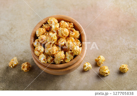 Bowl of delicious caramel popcorn surrounded by scattered pieces on a textured surface, perfect for snacking and sharing during movie nights 127705838