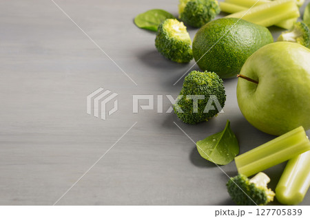 Fresh green vegetables including broccoli, celery, and green apple arranged artistically on a textured gray surface, showcasing healthy eating concepts 127705839