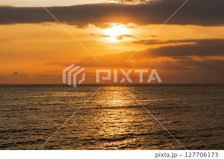 Golden sunset light reflects beautifully on dark ocean waves under dramatic clouds 127706173