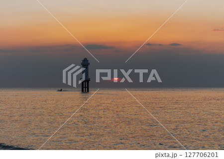 White lighthouse structure stands in the tranquil sea at golden hour sunset 127706201