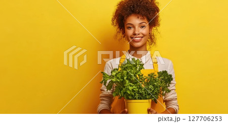 Woman with curly hair holds a pot of fresh green herbs in front of a vibrant yellow background showcasing her love for gardening and healthy living 127706253