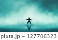 Martial artist performs in silhouette on calm water at dawn surrounded by misty fog creating a serene atmosphere with reflection 127706323