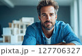 Young man with a beard poses confidently in a modern workspace, showcasing creativity and approachability while surrounded by architectural models 127706327