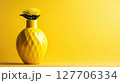 Bright yellow vase with a daisy flower against a vibrant yellow backdrop creating a cheerful and inviting atmosphere 127706334
