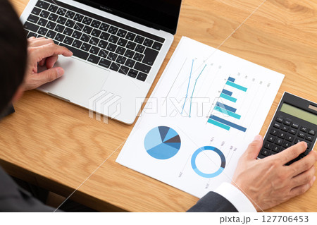 デスクでグラフを見ながらパソコン仕事をするスーツを着たミドル男性ビジネスマン 127706453