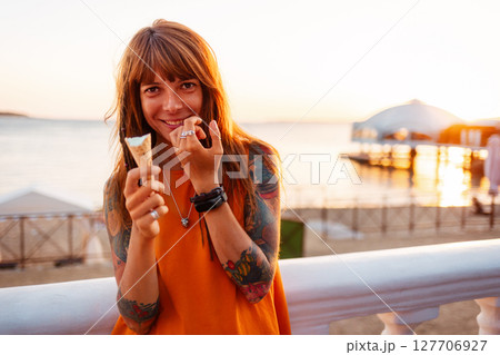 Portrait of young happy beautiful Caucasian woman with tattoos holds ice cream and looking at camera. Concept of freedom and psychology Portrait of young happy beautiful Caucasian woman with tattoos holds ice cream and looking at camera. Concept of freedom and psychology 127706927