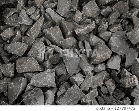 A close-up view of a textured background made of small, irregularly shaped dark gray stones.  127707472