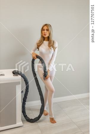 Woman in white suit for LPG massage. Anti-cellulite body care concept. Gray background Woman in white suit for LPG massage. Anti-cellulite body care concept. Gray background 127707501