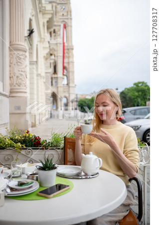 Woman enjoying tea at outdoor cafe near historic European building facade Woman enjoying tea at outdoor cafe near historic European building facade 127708317