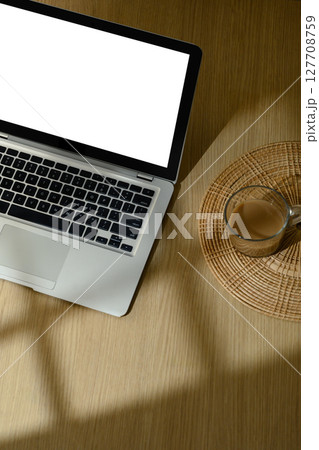 Overhead view of laptop with blank screen and coffee cup on wooden table in morning sunlight 127708759