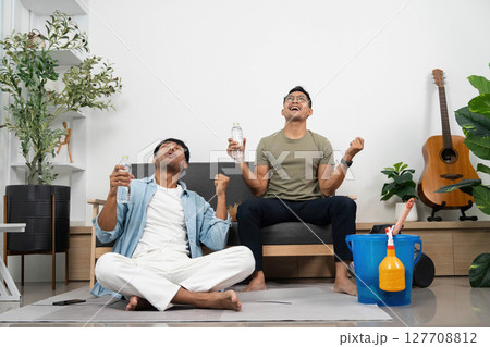 Celebration of Friendship. Two young men joyfully raising water bottles after cleaning their space. 127708812