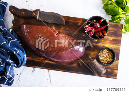 Raw Beef liver meat on wooden board with peppers Raw Beef liver meat on wooden board with peppers 127709323
