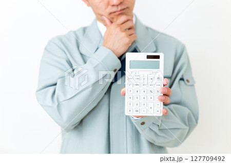 グリーンの作業服を着て電卓を持って悩むミドル男性ビジネスマン 127709492