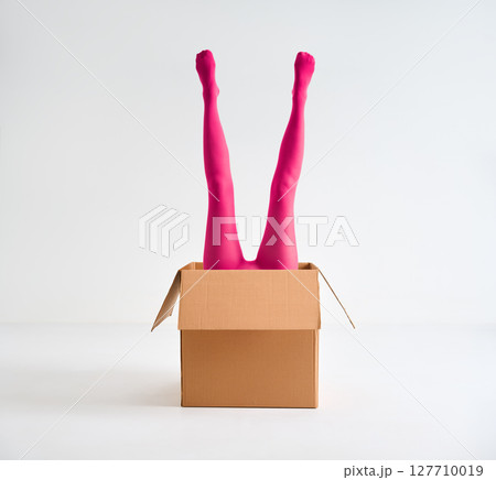 Female legs in bright pink tights raised up from open cardboard box Female legs in bright pink tights raised up from open cardboard box 127710019