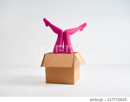 Female legs in bright pink tights raised up from open cardboard box Female legs in bright pink tights raised up from open cardboard box 127710020