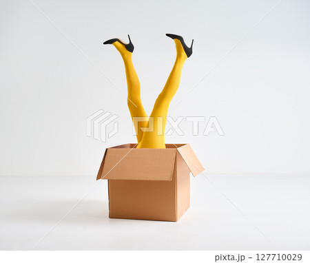 Female legs in yellow tights and high heels shoes raised up in open cardboard box Female legs in yellow tights and high heels shoes raised up in open cardboard box 127710029