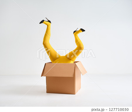 Female legs in yellow tights and high heels shoes raised up in open cardboard box Female legs in yellow tights and high heels shoes raised up in open cardboard box 127710030