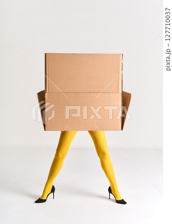 Woman in yellow tights and black high heels hidden under oversized cardboard box 127710037